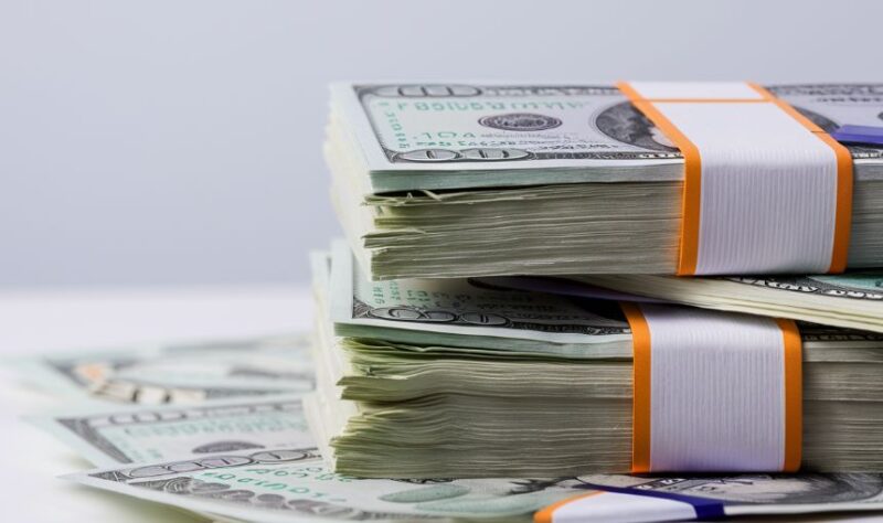 Dva sloลพena bunta ameriฤkih dolara povezana gumicama, postavljena jedan na drugi.