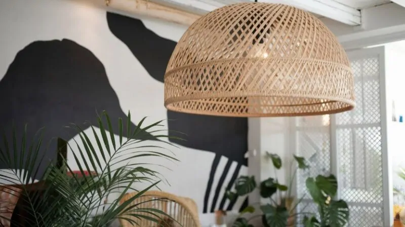 Boho stil luster sa velikim pletenim abažurom od ratana, visi u modernom prostoru ukrašenom biljkama i crno-belim muralom na zidu, pružajući prirodan i opušten ambijent.