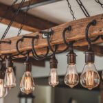 Rustični drveni luster sa Edison sijalicama koje vise sa debelog drvenog greda, sa metalnim kukama i lancima za industrijski izgled.
