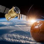 Slika prikazuje satelit u orbiti iznad Zemlje sa starinskom kožnom fudbalskom loptom u blizini, simbolizujući prvi satelitski prenos fudbalske utakmice.