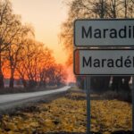 Putokaz za selo Maradik pri zalasku sunca, sa natpisima na srpskom i mađarskom jeziku, okružen golim drvećem i putem prekrivenim opalim jesenjim lišćem.