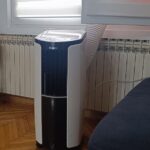 Pokretna klima uređaj GREE postavljena u dnevnoj sobi pored grejnog radijatora, s izduvnom cevkom kroz prozor.
