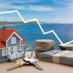 Prikaz investicije u nekretninu na moru, sa modelom kuće, hrpom novca i silaznom linijom koja označava fluktuacije na tržištu