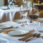 Elegantno postavljen sto u restoranu sa čašama za vino, tanjirima i priborom za jelo na belom stolnjaku, koji stvara sofisticiranu atmosferu za obedovanje.