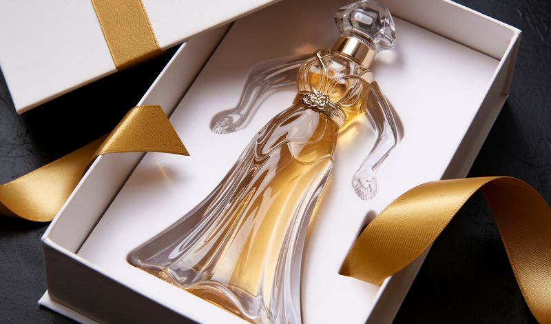 Luksuzni parfem u elegantnoj boฤici oblika veฤernje haljine, upakovan u poklon kutiju sa zlatnom trakom.