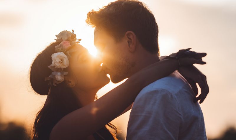 Zaljubljeni par razmenjuje poljubac pri zalasku sunca, dok topli zraci stvaraju romantiฤnu atmosferu.