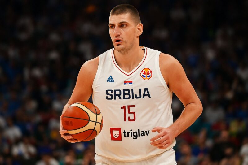 Nikola Jokić u akciji, drži košarkašku loptu u rukama, noseći dres Srbije sa brojem 15 i natpisom 'SRBIJA'