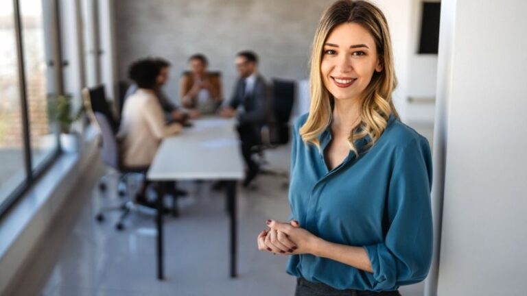 Nasmejana poslovna žena u kancelariji dok tim u pozadini održava poslovni sastanak