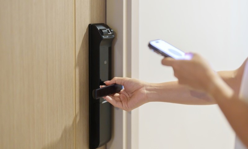 Ruka koja koristi pametni telefon za otvaranje digitalne brave na vratima apartmana