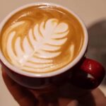 Šoljica kapućina sa latte art motivom koju drži barista u kafiću
