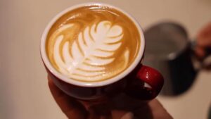 Šoljica kapućina sa latte art motivom koju drži barista u kafiću