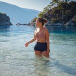 Žena u dvodelnom kupaćem kostimu stoji u plitkoj vodi na mirnoj plaži