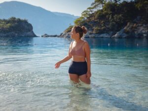 Žena u dvodelnom kupaćem kostimu stoji u plitkoj vodi na mirnoj plaži