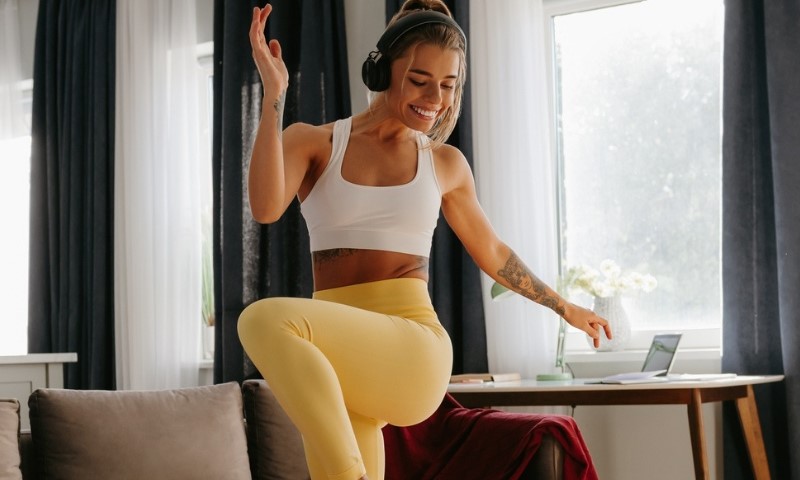 Nasmejana mlada žena sa slušalicama pleše tokom časa aerobika kod kuće