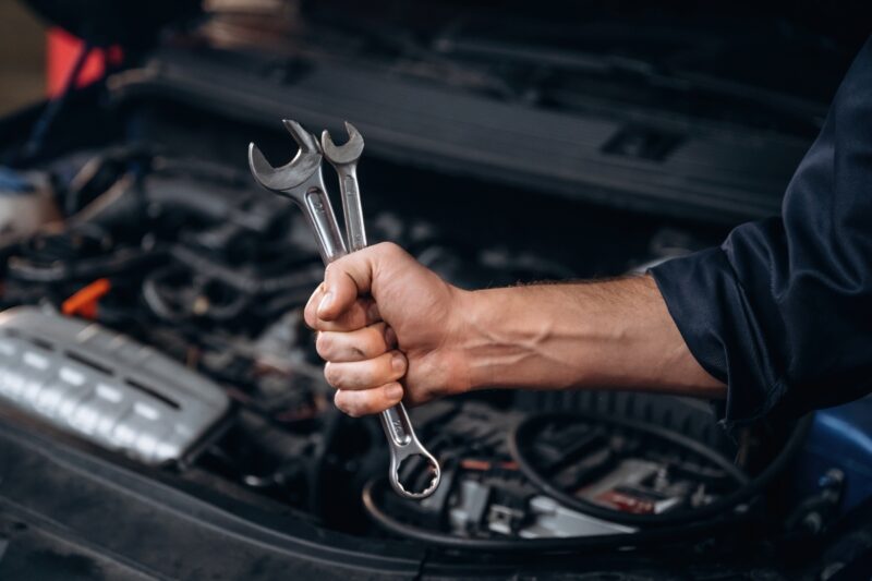 prikaz majstora koji drži alat u ruci i automobila u pozadini