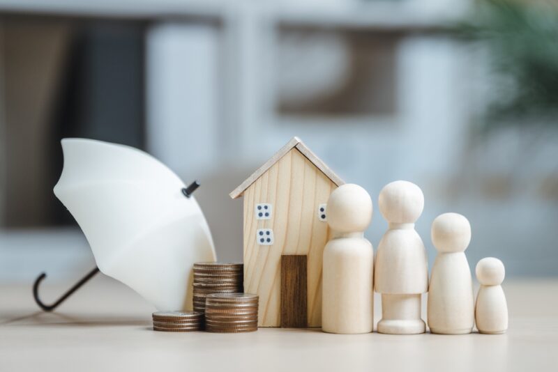 Porodica simbolično prikazana figurama uz kuću, novac i kišobran kao znak finansijske zaštite