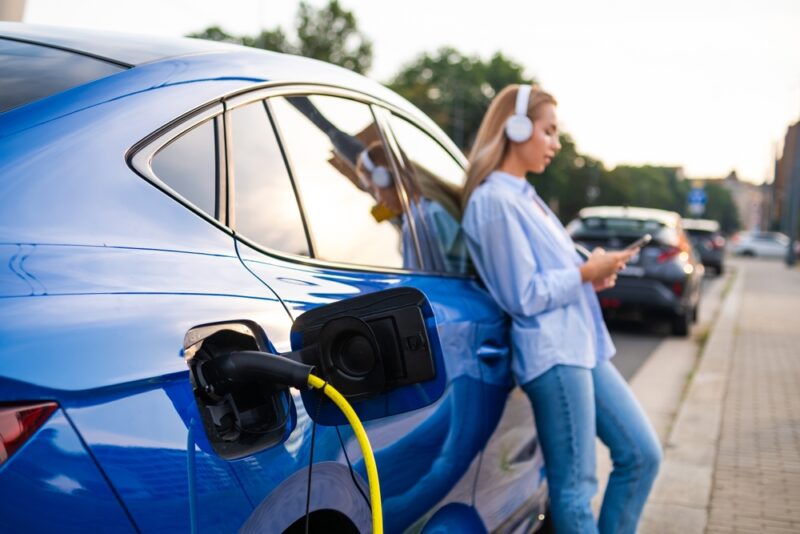 Vozač koristi mobilni telefon dok se električni automobil puni na pametnom EV punjaču.