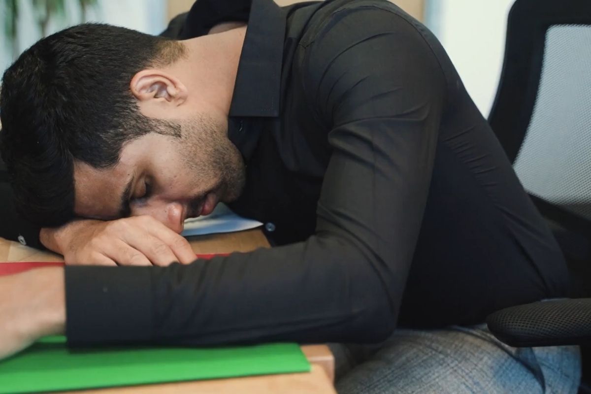 momak leži na kancelarijskom stolu vidno nezadovoljan poslom