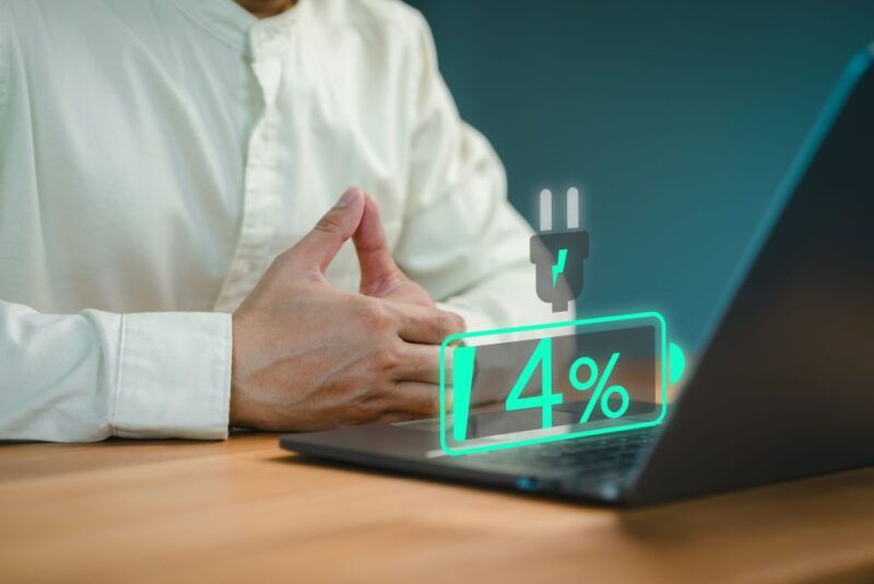 Muškarac koristi laptop sa prikazanim nivoom baterije od 4%, što ukazuje na potrebu za punjenjem uređaja